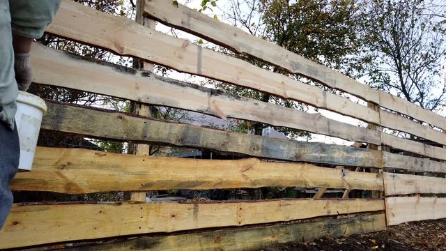Bearded man paints a new wooden fence. Processing a new wooden fence. Painting a new fence.