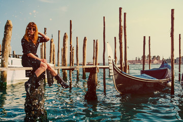 Redhead girl with long black dress, sunglasses and cowboy boots sitting on Gondola boards in Venice © Roberto Vivancos