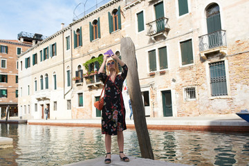 Fototapeta na wymiar Caucasian redhead woman with floral dress taking photos with phone in Venice