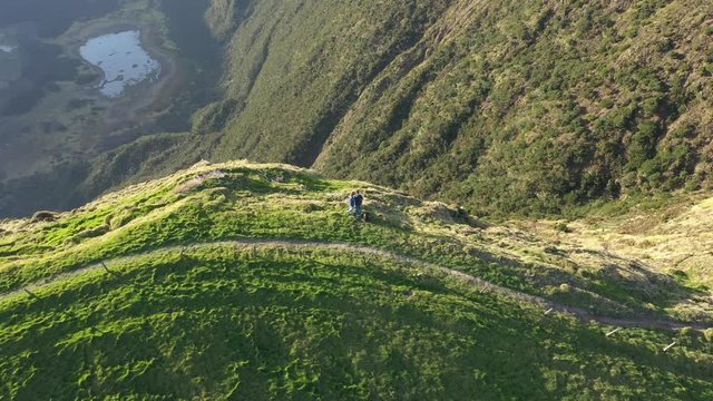 Man and woman on the top of volcano look into huge green caldera. Aerial of Faial, Azores