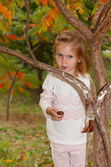 Adorable baby girl holds snail, playing in a sunny park under a tree with yellow leaves, hiding behind tree
