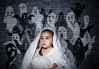 Scared girl with pillow hiding under blanket