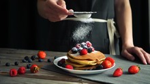 Sugar powder being poured over pancakes beautifully served with berries. Food art. Dessert and breakfast concept. Closeup shot. pastry pour sugar.