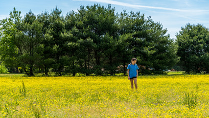 Teen girl standing in large field with yellow flowers and trees in the background