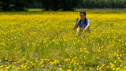 Fototapeta premium Teen girl with braids sitting in large field with yellow flowers