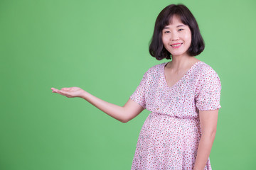 Portrait of happy Asian pregnant woman showing something