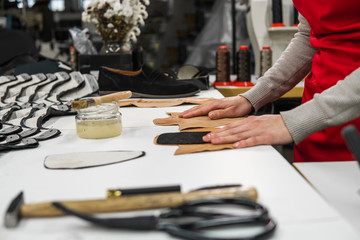 Shoemaker is adding glue with a brush to some pieces of leather that will be used to make shoes. The cobbler is working on his desk in his workshop.