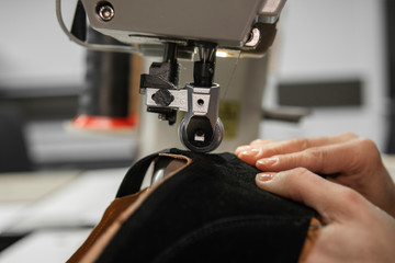 Sewing machine in a leather workshop in action with hands working on a leather details for shoes. Women's hands with sewing machine at shoes factory.