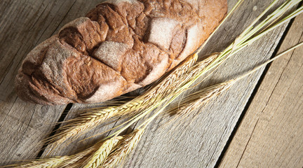 rustic crusty bread and wheat ears on a dark wooden table
