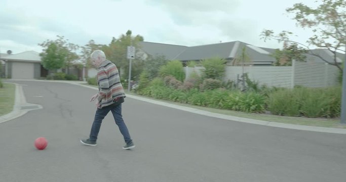 Elderly woman plays street basketball, she is dribbling and bouncing the ball before passing it. The ball is thrown back to the woman and she has to run after it