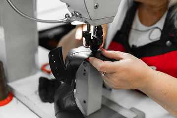 Sewing machine in a leather workshop in action with hands working on a leather details for shoes. Women's hands with sewing machine at shoes factory.