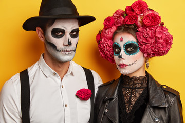 Participants of parade in Mexico, prepare to most popular holiday, wears skull makeup, black and white clothes, isolated over yellow background. Serious vampires celebrate Halloween together © wayhome.studio