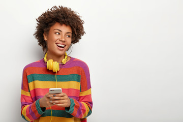 Modern communication concept. Positive woman laughs joyfully, uses up to date cellular for chatting...
