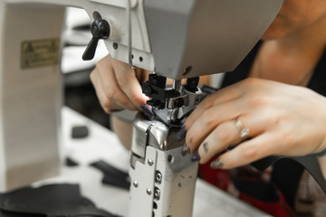 Sewing machine in a leather workshop in action with hands working on a leather details for shoes. Women's hands with sewing machine at shoes factory.