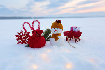 Funny snowman with sledges and colorful boxes with presents. Garlands enlighten the snow. New Year...