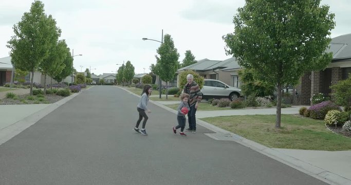 Elderly woman playing street basketball with two young children, The old woman dribbles and bounces the ball before handing off to the small before who tries to kick it