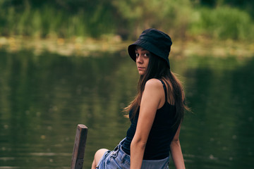 girl in panama hat posing on a pier by a lake in the woods