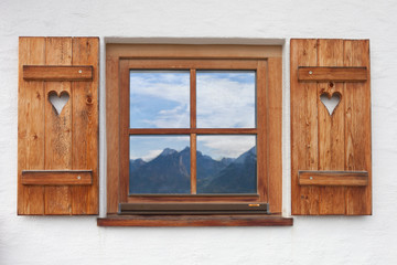 hölzernes rustikales Fenster, offene Läden, Spiegelung der Berglandschaft und Himmel