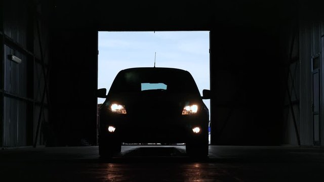 silhouette of car with yellow bright headlights turning off on pit stop in large garage hangar for maintenance