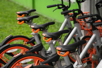 Street transportation orange hybrid rent bicycles with electronic form of payment for traveling around the city stand in row on rental network parking lot waiting for cyclists to make bike trip.