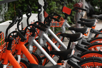 Fototapeta na wymiar Street transportation orange hybrid rent bicycles with electronic form of payment for traveling around the city stand in row on rental network parking lot waiting for cyclists to make bike trip.