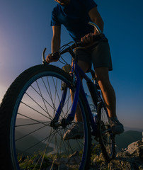 Close up silhouette of an athlete (mountain biker) riding his bike on rocky mountains.