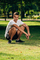 Fototapeta premium Fit man warming up doing squats stretching arms forward outdoors