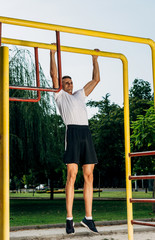 Exercising fitness athlete man training pull ups in nature park