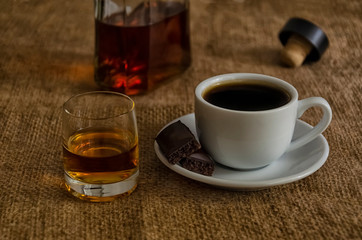White cup of coffee and cognac in a burlap glass on a table.