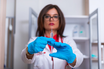 Close up od a female doctor ( nurse ) holding a syringe while standing in a medical office