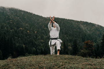 Martial art of karate, a man in a kimono with black belt trains on the mountain,free space.