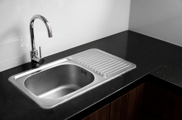 Close up on modern kitchen metal faucet and metal kitchen sink.