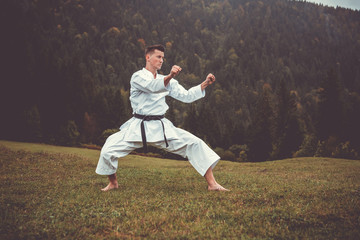 Martial art of karate, a man in a kimono with black belt trains on the mountain,free space.