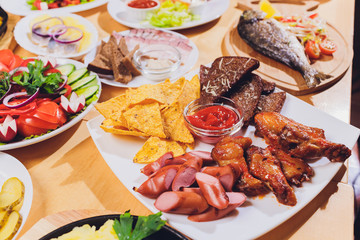Dining table with a variety of snacks and salads. Salmon, olives, wine, vegetables, grilled fish...