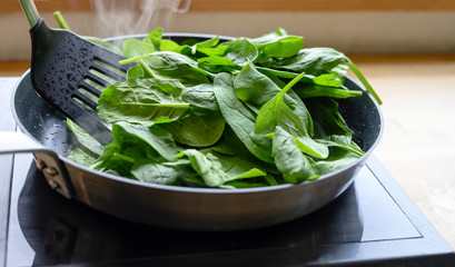 frying fresh spinach in a pan on the stove, healthy cooking at home concept