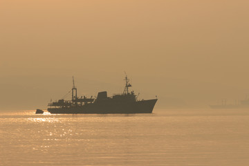 Fototapeta premium A ship sails into the distance in the early morning fog at dawn.