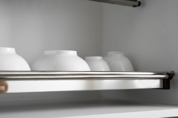 Dish drying metal rack with big nice white clean plates. Traditional comfortable kitchen. Open white dish draining closet with wet dishes of glass and ceramic, plates, bowls drying inside on rack.