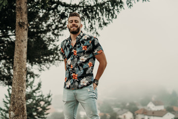 Young man with beard and flowered shirt posing in nature