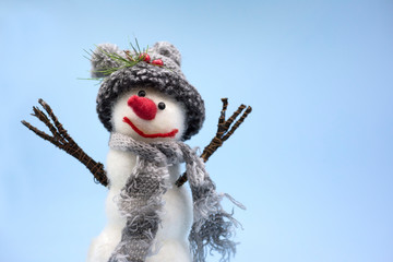 Portrait of a toy snowman on a blue background. Snowman in a gray hat and in a gray scarf close-up. Place for text