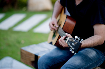 Picture of a guitarist, a young man playing a guitar while sitting in a natural garden,music concept