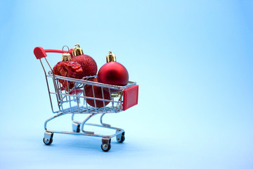 Miniature model supermarket trolley with red Сhristmas balls inside on a blue backgound. New Year discounts and sales concept