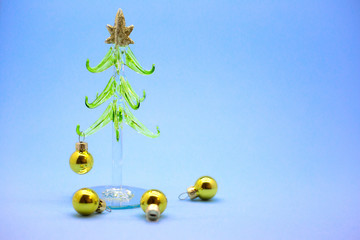 Miniature Christmas tree made of glass with golden balls isolated on a blue background. New Year card. Place for text