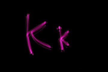 Fototapeta na wymiar Long exposure photograph of the letter k in upper case and lower case in pink neon colour in an abstract swirl, parallel lines pattern against a black background. Light painting photography.