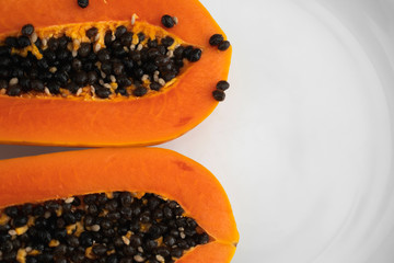 Half cut ripe papaya with seed on a white plate. Slices of sweet papaya with a white background. Halved papayas. Healthy exotic fruits. Vegetarian food.