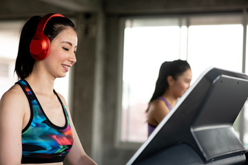 Side View Of Smiling Young Woman Wearing Red Headphones While Exercising On Treadmill In Gym