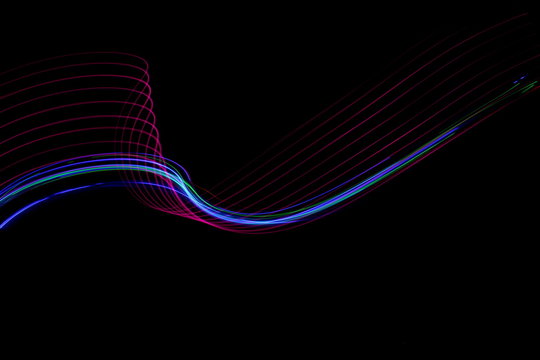 Long exposure photograph of neon pink and blue colour in an abstract swirl, parallel lines pattern against a black background. Light painting photography.