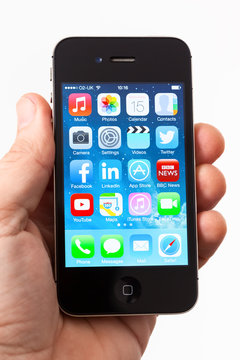 BATH, UK - JANUARY 15, 2014: A man's hand holding an Apple iPhone 4s installed with iOS 7 software. Shot in close-up against a plain background with various App icons on the smartphone's home screen.
