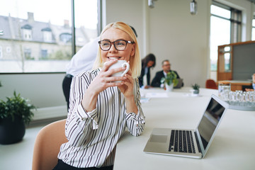 Smiling businesswoman enjoying a coffee while woring in an offic