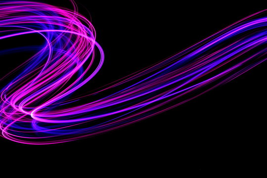 Long exposure photograph of neon pink and purple colour in an abstract swirl, parallel lines pattern against a black background. Light painting photography.