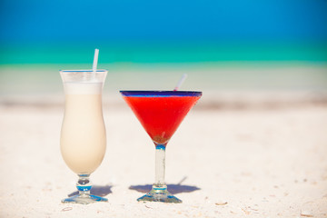 Two cocktails: pina colada and strawberry margarita on white sand beach